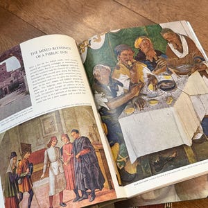 May include: Open book with illustrations of historical scenes. One page features text titled "THE MIXED BLESSINGS OF A PUBLIC INN." The other page shows a colorful depiction of people at a table. The book is open on a wooden surface.