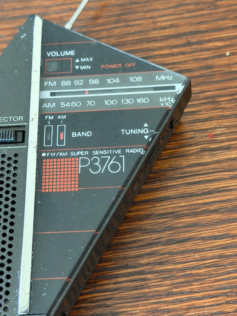 May include: A vintage black and silver FM/AM radio with a tuning dial and frequency display. The radio features a volume control, band selection, and the text "P3761". The radio's frequency range is displayed in MHz and kHz.