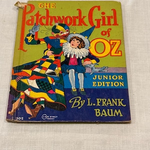 Może przedstawiać: Vintage książka zatytułowana "The Patchwork Girl of Oz" z kolorowymi ilustracjami. Okładka przedstawia postać z patchworku i dziecko w niebieskim stroju. Widoczne jest również nazwisko autora, L. Frank Baum.