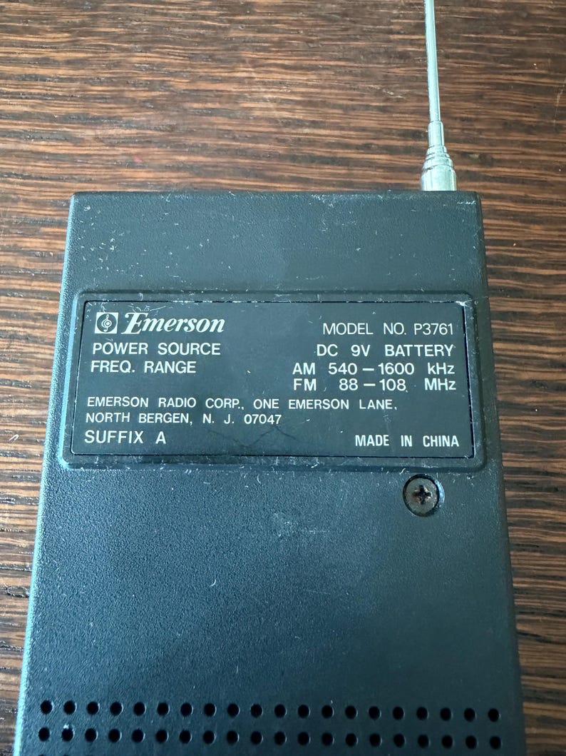 May include: Black Emerson radio with a silver antenna. The radio has the following text: "POWER SOURCE", "FREQ. RANGE", "MODEL NO. P3761", "DC 9V BATTERY", "AM 540-1600 kHz", "FM 88-108 MHz", "MADE IN CHINA".