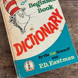 Puede incluir: Una portada de libro vintage con el personaje del Gato en el Sombrero de la popular serie de libros para niños. El libro se titula "The Cat in the Hat Beginner Book Dictionary" y está escrito por P.D. Eastman. La portada es de color amarillo brillante con acentos rojos y azules.