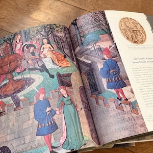 May include: Open book with medieval illustrations. The artwork depicts figures in period clothing, including men in blue tunics and red hats, and women in long gowns. The illustrations are colorful and detailed, with scenes of courtly life and architecture.