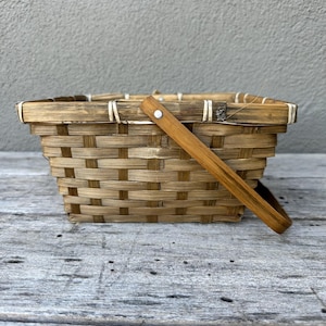 May include: A brown woven basket with a wooden handle. The basket is made of natural materials and has a rectangular shape.