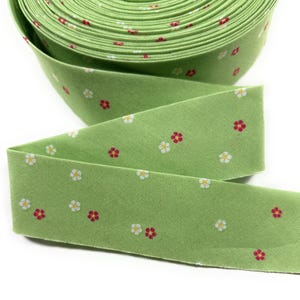 May include: A roll of light green fabric bias tape with a repeating pattern of small white and red flowers. The tape is unrolled, showing the floral pattern and the texture of the fabric. This tape is suitable for sewing and crafting projects.