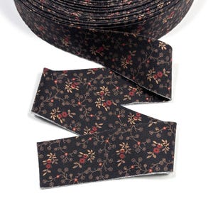 May include: A roll of black fabric ribbon with a floral pattern. The ribbon features small red and tan flowers with green stems and leaves. The ribbon is on a white background.