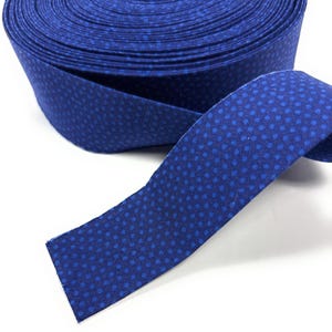 May include: A roll of blue fabric with white polka dots. The fabric is folded and rolled up, with a section of the fabric unrolled to show the pattern.