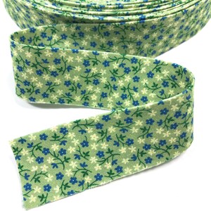 May include: A roll of green fabric with a white and blue floral print. The fabric is folded and has a raw edge.