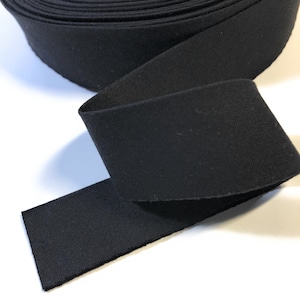 May include: A roll of black elastic band material. The band is a solid black color and appears to be made of a woven fabric. The material is rolled up, with a portion unrolled and lying flat.