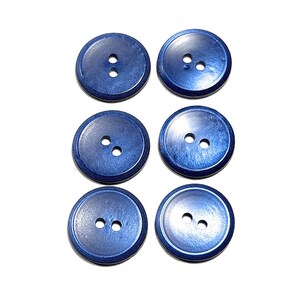 May include: A set of six circular buttons in a deep metallic blue finish. Each button features a smooth, slightly recessed center with two holes positioned vertically in the middle. The buttons have a consistent, polished appearance.