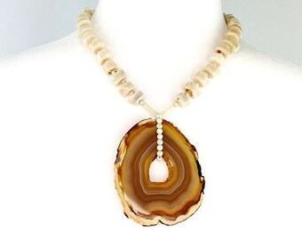 May include: A necklace with a large, brown agate pendant and white beads. The agate is a slice of a geode, with a hole in the center.