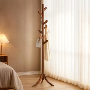 May include: A wooden coat rack with a tree-like design. The rack has multiple leaf-shaped pegs for hanging clothes and accessories. A white purse and a cream-colored dress hang from the rack. The rack stands on a three-legged base.