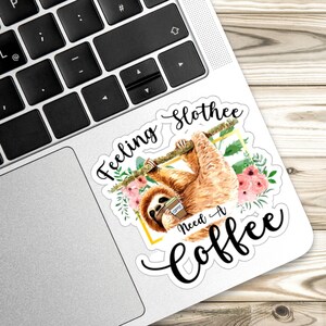 May include: A white sticker featuring a watercolour illustration of a sloth hanging from a branch with a cup of coffee. The text "Feeling Slothee Need A Coffee" is written in black cursive font.