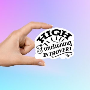 Könnte beinhalten: Weißer Aufkleber mit schwarzem Text, der "HIGH functioning INTROVERT" lautet. Der Text ist in einer stilisierten Schriftart gehalten und hat ein Sonnenstrahlendesign dahinter.