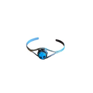 May include: A silver cuff bracelet with a turquoise stone centerpiece. The bracelet has a twisted design on the band and a decorative setting around the turquoise stone. The turquoise stone is a bright blue color.