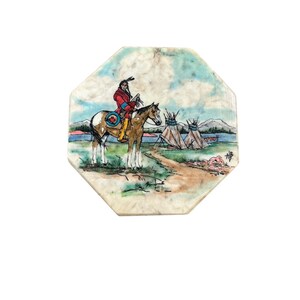 May include: An octagonal coaster featuring a Native American on horseback, rendered in a watercolor style. The rider wears a red jacket and sits atop a brown and white horse. The background depicts teepees, a lake, and a cloudy sky.