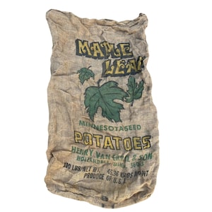 May include: A tan hessian sack featuring the text MAPLE LEAF, MINNESOTASEED POTATOES, HENRY VAN ERKEL & SON, HOLLANDALE, MINN. 56045, 100 LBS. NET WT. 45.36 KROS NET WT. PRODUCE OF U.S.A. with green maple leaf illustrations printed on the front.