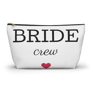 Puede incluir: Bolsa blanca con cremallera con texto negro que dice "BRIDE crew" y un pequeño corazón rojo.
