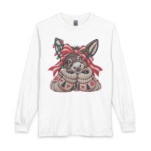 May include: A white long-sleeve shirt featuring a graphic of a brown donkey wearing a cream-coloured cable knit sweater with red hearts and green trees. The donkey has a red and white striped bow, holly berries, and string lights on its head.