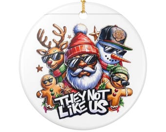 May include: A round Christmas ornament featuring a festive design. The ornament showcases Santa Claus, a reindeer, a snowman, and gingerbread figures, all wearing sunglasses. The text "THEY NOT LIKE US" is displayed in a bold font. A gold string is attached for hanging.