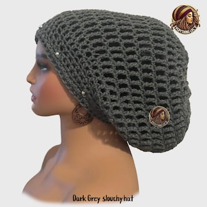May include: Dark gray slouchy hat with a crocheted open weave design. The hat is adorned with small silver-colored embellishments and a circular pin with a woman's profile. The text "Everything Loc'd" is on the pin.
