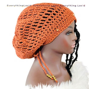 May include: A crocheted orange beanie with gold beads. The beanie has a drawstring and is designed to be worn with locs.