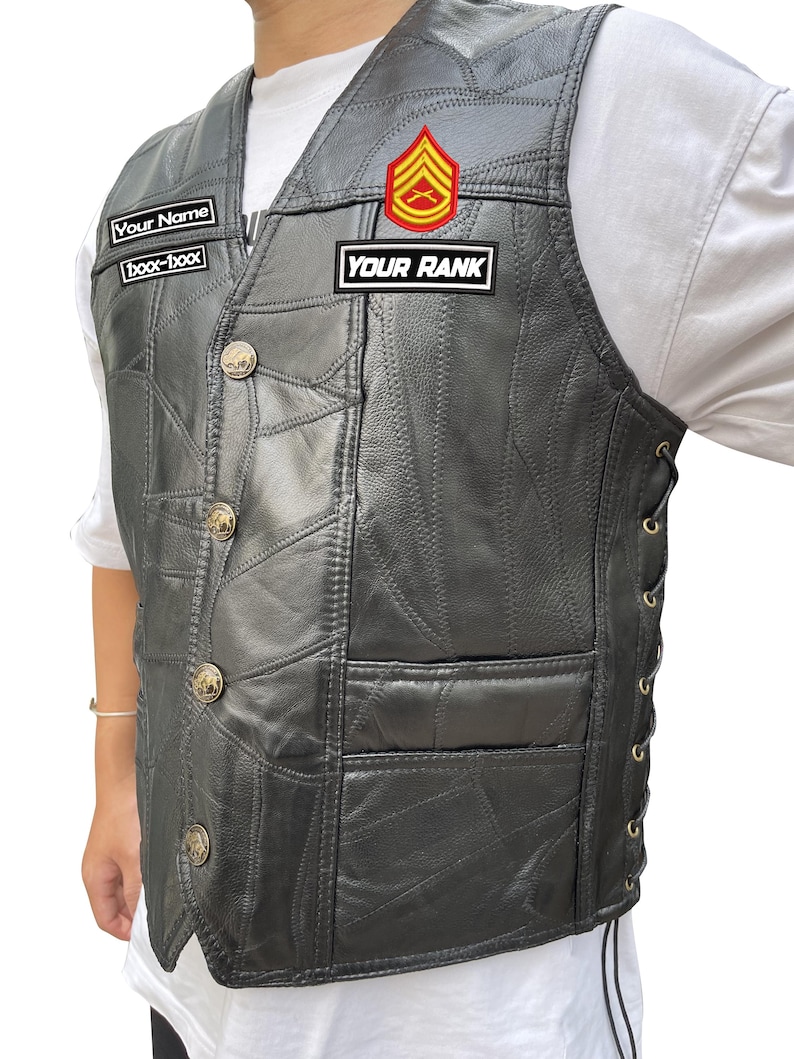 K&ouml;nnte beinhalten: Schwarze Lederweste mit Patchwork-Design, goldenen Kn&ouml;pfen und seitlicher Schn&uuml;rung. Die Weste hat zwei Aufn&auml;her mit der Aufschrift "Your Name" und "Your Rank" sowie ein rot-goldenes Emblem.