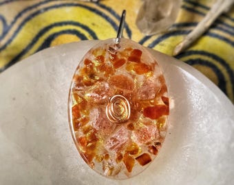 May include: A clear oval pendant with a copper wire swirl and red and gold flecks of stone inside.