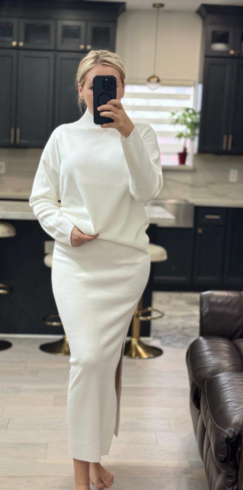 May include: A white turtleneck sweater and matching skirt set. The sweater has long sleeves and a relaxed fit. The skirt is a midi length and has a slit on the side.