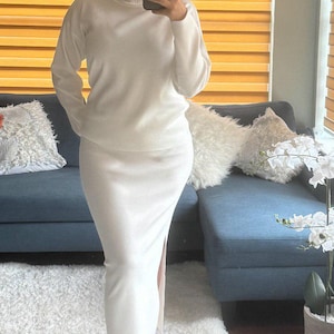 May include: A white knit sweater and matching skirt set. The sweater has a turtleneck and long sleeves. The skirt is a midi length with a slit on the side.