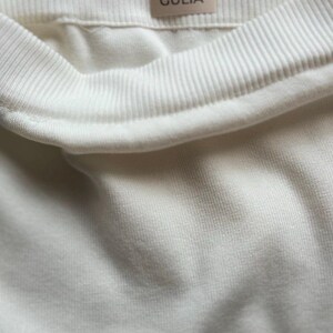 May include: White ribbed knit fabric with a white label that says "GULIA" on it.