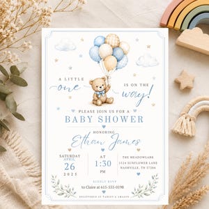 May include: A rectangular baby shower invitation card featuring a watercolor illustration of a brown teddy bear holding a cluster of blue, cream, and plaid balloons. The text reads A LITTLE one IS ON THE WAY! PLEASE JOIN US FOR A BABY SHOWER HONORING Ethan James SATURDAY APRIL 26 2025 AT 1:30 PM THE MEADOWLARK 1524 SUNFLOWER LANE NASHVILLE, TN 37204 KINDLY RSVP to Claire at 615-555-0198 REGISTERED AT TARGET & AMAZON.
