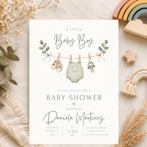 Puede incluir: Una tarjeta de invitaci&oacute;n blanca para baby shower con una ilustraci&oacute;n en acuarela de un tendedero con zapatos de beb&eacute;, un mameluco a rayas y un chupete. El texto incluye A LITTLE Baby Boy, BABY SHOWER, en honor a Daniela Martinez.