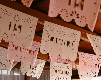 May include: A sparkling, blush-pink ball gown on a mannequin. The dress features a fitted, embellished bodice and a voluminous skirt with a long train. Decorative paper banners with the name "Camila" hang above.