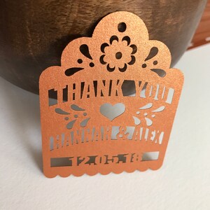 Puede incluir: Etiqueta de corte l&aacute;ser color cobre con las palabras "THANK YOU" y los nombres "HANNAH & ALEX" junto con una fecha. La etiqueta presenta un dise&ntilde;o floral y de coraz&oacute;n decorativo, ideal para recuerdos de boda.