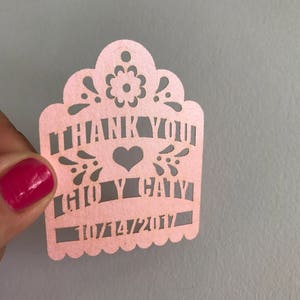 Puede incluir: Un recorte de papel rosa con las palabras "THANK YOU" y "CHLOE & CAIN" con un s&iacute;mbolo de coraz&oacute;n. La fecha "07/14/2017" tambi&eacute;n est&aacute; recortada. El borde superior tiene un dise&ntilde;o floral decorativo.