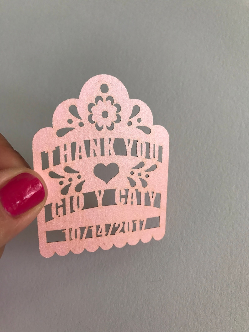 Puede incluir: Un recorte de papel rosa con las palabras "THANK YOU" y "CHLOE & CAIN" con un s&iacute;mbolo de coraz&oacute;n. La fecha "07/14/2017" tambi&eacute;n est&aacute; recortada. El borde superior tiene un dise&ntilde;o floral decorativo.