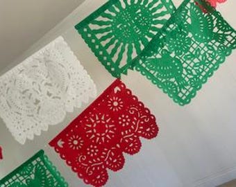 May include: A festive banner featuring cut-out paper flags in white, red, and green. The flags display intricate patterns of sunbursts, flowers, and other decorative shapes. The banner is likely used for celebrations or decorations.