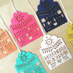 Puede incluir: Una colecci&oacute;n de etiquetas decorativas coloridas con la frase "I Shake for a Kiss" recortada. Las etiquetas son de varios colores, incluyendo rosa, azul, blanco y amarillo, y est&aacute;n ensartadas con hilo blanco.