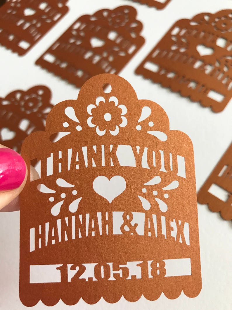 Puede incluir: Etiqueta de corte l&aacute;ser color cobre con recortes decorativos florales y de coraz&oacute;n. La etiqueta dice "THANK YOU HANNAH & ALEX 12-05-18". La etiqueta tiene un borde festoneado y un peque&ntilde;o agujero en la parte superior.