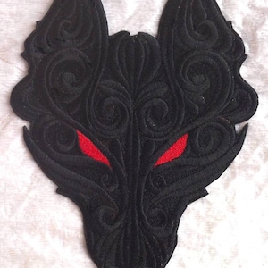 May include: Black embroidered patch of a wolf's head with intricate details and red eyes.