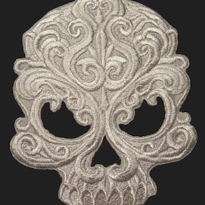 May include: A white embroidered skull patch with intricate floral designs. The skull is detailed with eye sockets, a nose, and a mouth.