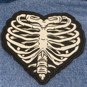 May include: A black and white embroidered patch shaped like a heart with a ribcage design.