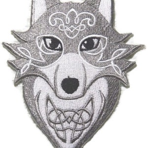 May include: A gray embroidered iron-on patch of a wolf's head with intricate white designs and black eyes.