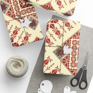 Könnte beinhalten: Drei Geschenkboxen, die in cremefarbenes Papier mit einem roten und schwarzen geometrischen Muster verpackt sind. Die Boxen sind mit Schnur gebunden und haben weiße Papieretiketten.