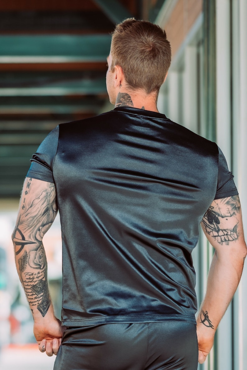 May include: Black satin t-shirt and shorts set. The short-sleeved top has a crew neck and the shorts have a comfortable fit. The fabric has a shiny, smooth texture. The model has tattoos on both arms.