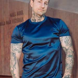 May include: A navy blue athletic t-shirt and shorts set. The short-sleeved shirt has a small logo on the chest. The set is made of a shiny, silky material. The person in the image has tattoos on their arms and neck.