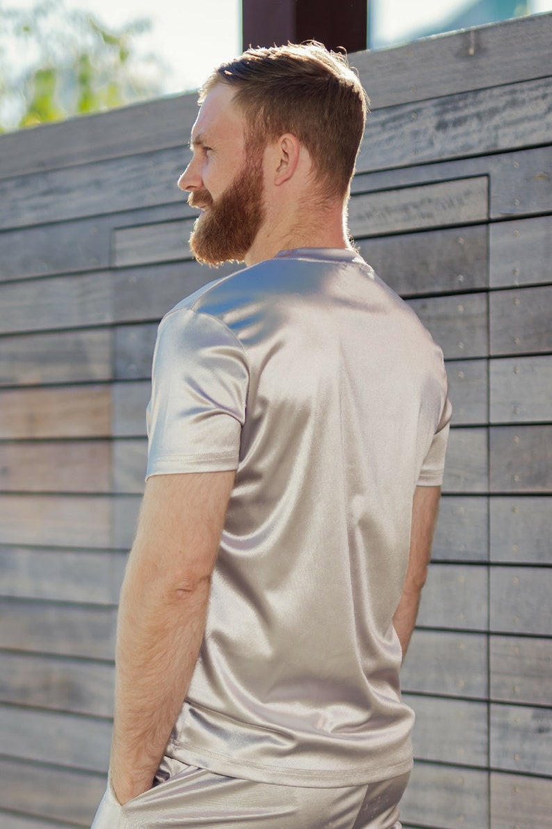 May include: A light silver-colored short-sleeved t-shirt and matching shorts. The fabric has a satin-like sheen. The person is standing in front of a wooden wall.