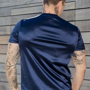 May include: Navy blue satin t-shirt and matching shorts. The short-sleeved top has a crew neck and a smooth, shiny texture. The outfit is a solid color and appears to be made of a lightweight material. The model is facing away from the camera.