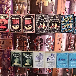 May include: A set of book-themed earrings featuring classic novels such as "Animal Farm", "1984", "The Great Gatsby", "Little Women", "Wuthering Heights", "The Color Purple", and "The Adventures of Huckleberry Finn".