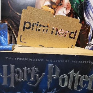 Peut inclure: Une paire de boucles d'oreilles Harry Potter bleues et blanches avec un marque-page doré qui dit "print mord".